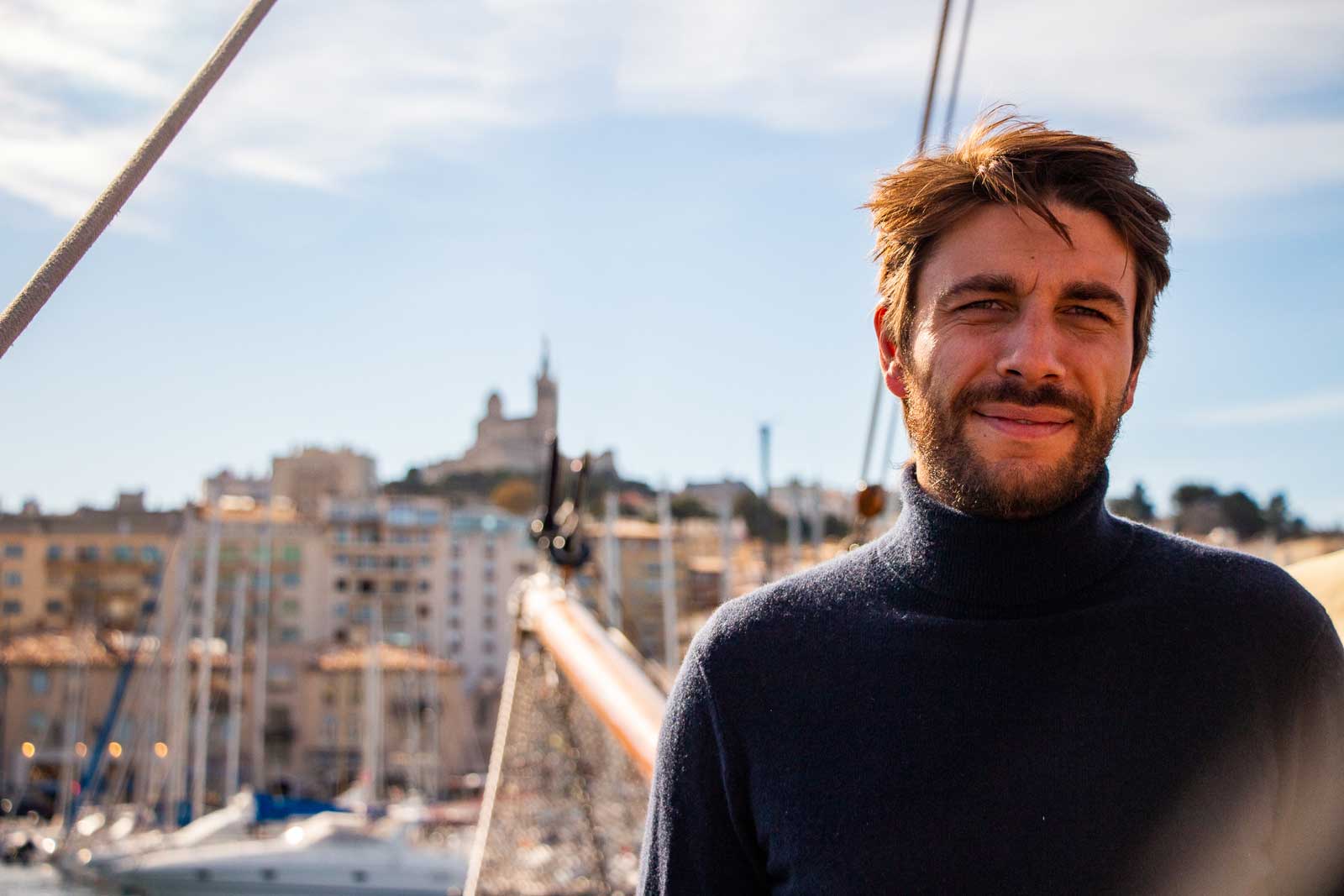 Mathieu Tambon, fondateur de Nautime, sur un voilier avec le Vieux Port de Marseille et Notre-Dame de la Garde en fond